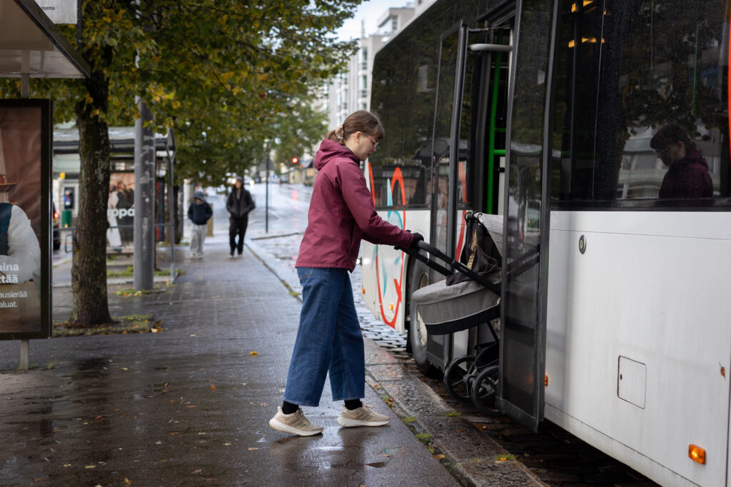 Nainen työntää lastenvaunuja bussiin.